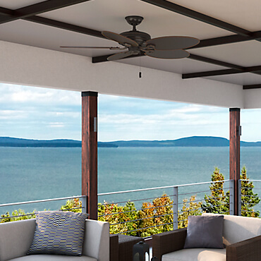 Pictured is a ceiling fan with rounded leaf-like blades and a pull-chain which is hanging over an outdoor patio area.